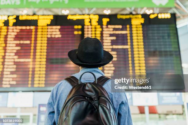 young man with hat and backpack looking at arrival departure board at the airport - arrival imagens e fotografias de stock