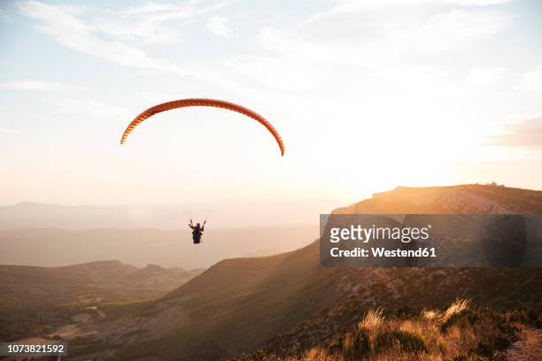spain, silhouette of paraglider soaring high above the mountains at sunset - paragliding stock pictures, royalty-free photos & images