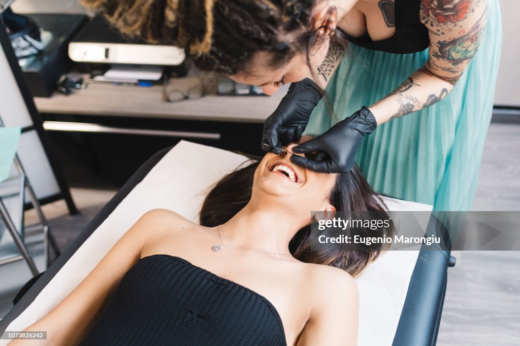 Tattooist piercing nose of customer in parlour