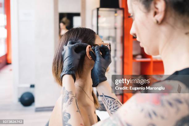 tattooist piercing ear of customer in parlour - piercing stock-fotos und bilder