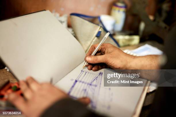 an artisan metal worker drawing up designs for a gate in a sketchbook - metal workshop photos et images de collection