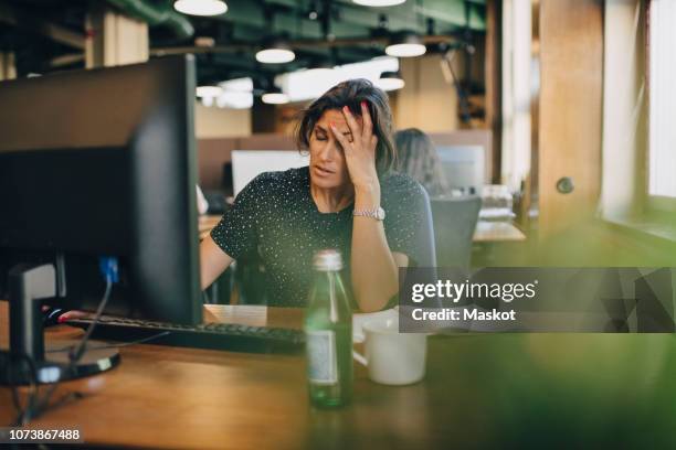 tired businesswoman with head in hand sitting at computer desk in office - belastung stock-fotos und bilder