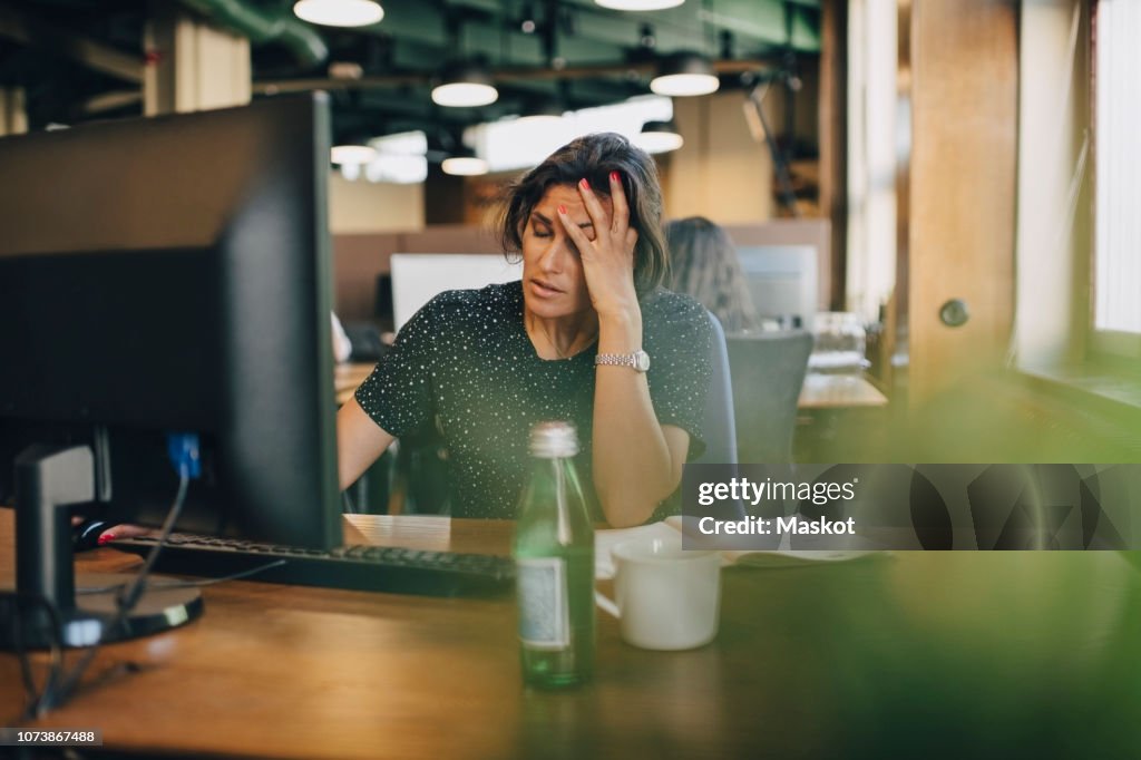 Tired businesswoman with head in hand sitting at computer desk in office