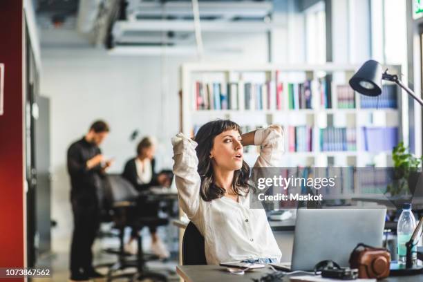 businesswoman looking away while sitting with hands behind head at desk in office - boredom 個照片及圖片檔