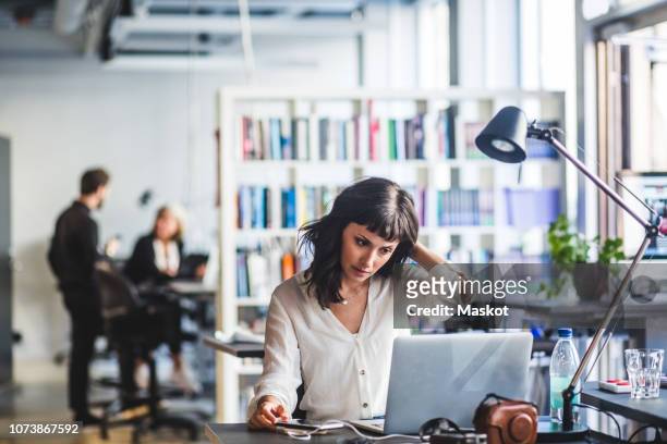 businesswoman looking at laptop while sitting in office - frustración fotografías e imágenes de stock