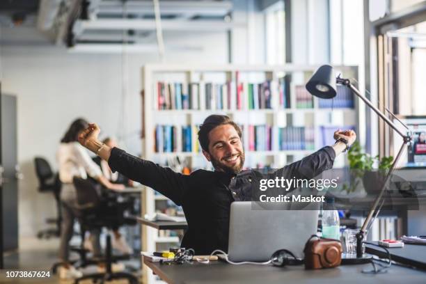 businessman sitting with arms outstretched at desk in office - man arms outstretched stock pictures, royalty-free photos & images