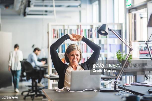 smiling businesswoman looking at laptop while sitting in office - woman business desk front laptop office fotografías e imágenes de stock