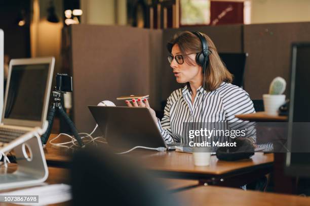 mature businesswoman wearing headphones while talking on mobile phone in office - conference phone stock pictures, royalty-free photos & images