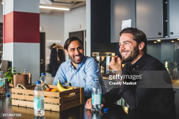 male colleagues smiling while sitting at table in office - fruit box stock-fotos und bilder