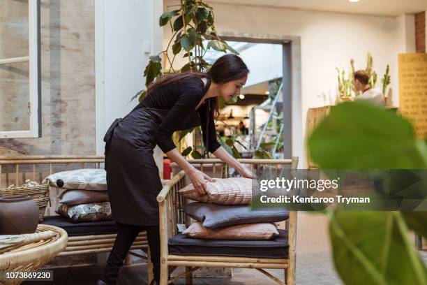 young saleswoman stacking cushions on chair at store - cushion stock-fotos und bilder