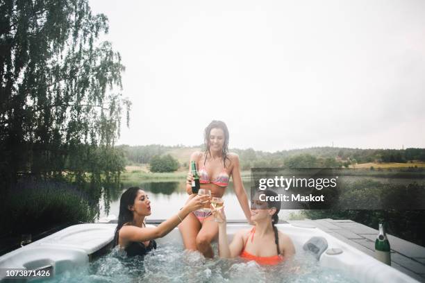 cheerful female friends toasting drinks in hot tub against clear sky during weekend getaway - hot tub party stock pictures, royalty-free photos & images