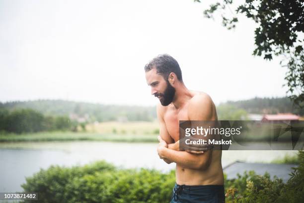 shirtless mid adult man shivering while standing in backyard during weekend getaway - beef stockfoto's en -beelden
