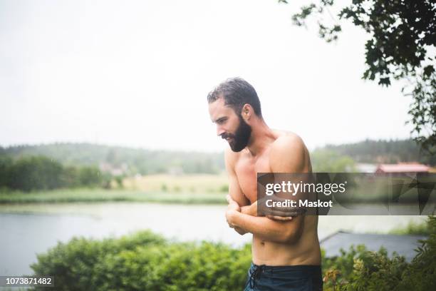 shirtless mid adult man shivering while standing in backyard during weekend getaway - shivering summer stock pictures, royalty-free photos & images