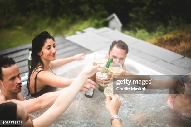 carefree male and female friends toasting drinks in hot tub during weekend getaway - hot tub party stock pictures, royalty-free photos & images