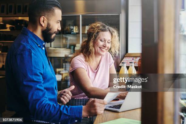 colleagues smiling with discussing over laptop at table in deli - scandinavia stock pictures, royalty-free photos & images
