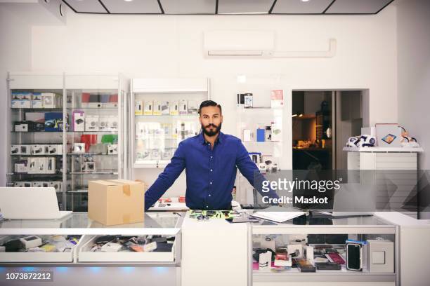 portrait of confident owner standing at counter in electronics store - salesman foto e immagini stock