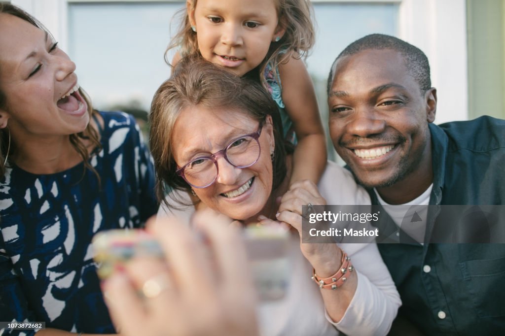 Cropped image of man showing mobile phone to happy family on porch