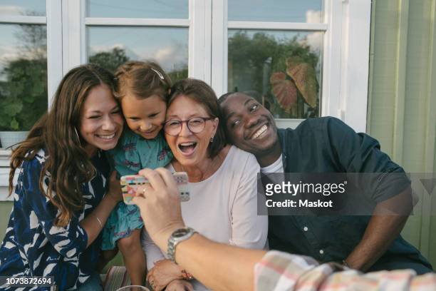 cropped image of man showing mobile phone to cheerful family on porch - dinner on the deck stock pictures, royalty-free photos & images