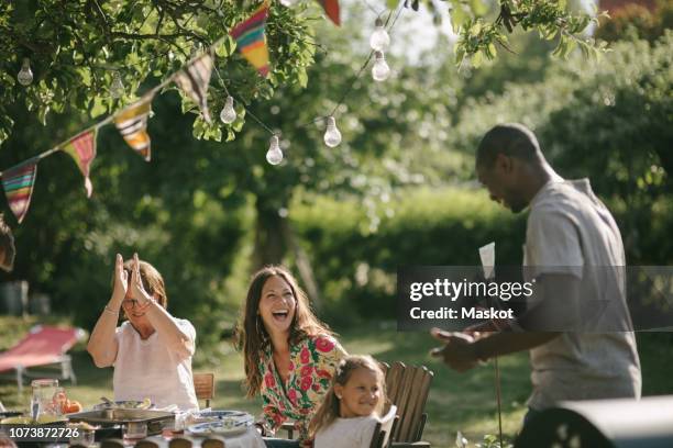 cheerful multi-generation family with lunch at table in backyard during garden party - patio party stock pictures, royalty-free photos & images