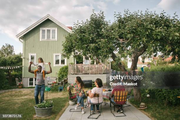 family looking at man carrying daughter on shoulders during garden party - sweden house stock pictures, royalty-free photos & images