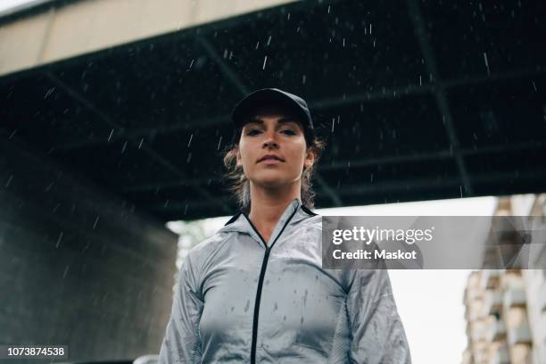 low angle portrait of female athlete standing against bridge during rainy season - low angle view portrait stock pictures, royalty-free photos & images