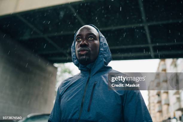 low angle view of sportsman looking away while standing against bridge during rainy season - black rain stock pictures, royalty-free photos & images