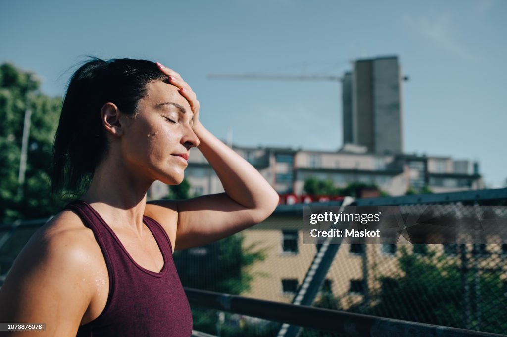 Exhausted sportswoman wiping sweat on forehead during sunny day