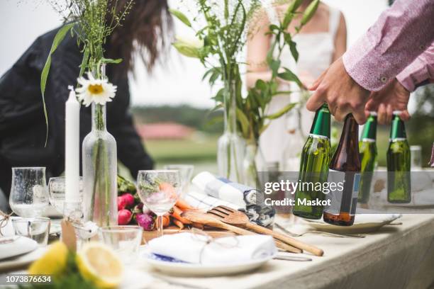 cropped image of man holding beer bottles at dining table during dinner party in backyard - table vase stockfoto's en -beelden