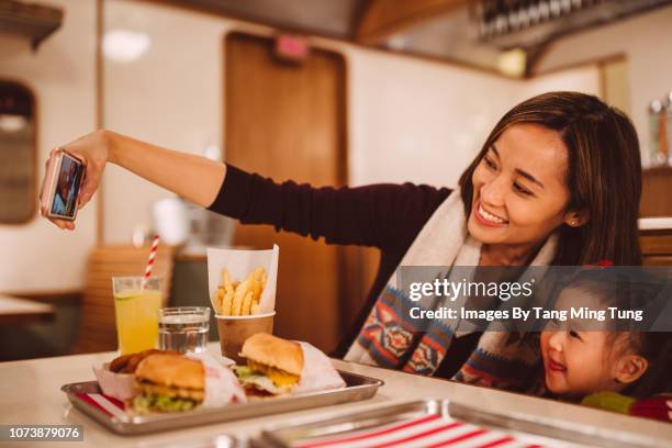 pretty young mom taking selfies with her lovely toddler girl joyfully in the restaurant - family eating potato chips stock pictures, royalty-free photos & images