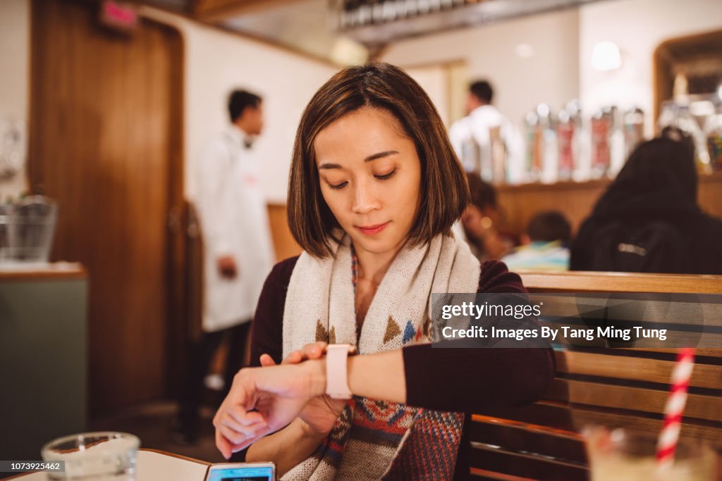 Pretty young lady waiting and using her smartwatch joyfully in the restaurant