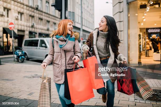 chicas llevando bolsas de compras - compras fotografías e imágenes de stock
