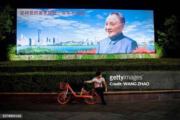 This picture taken on November 8, 2018 shows a man holding onto a sharing bicycle in front of a poster of Chinese former leader Deng Xiaoping in...