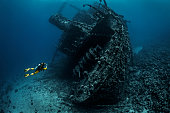 Scuba diver observing a large shipwreck completely rusted and overgrown lying underwater in the Red Sea