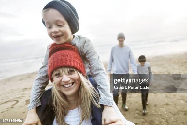 family on beach in winter, mother giving son piggyback - family looking at camera stock pictures, royalty-free photos & images