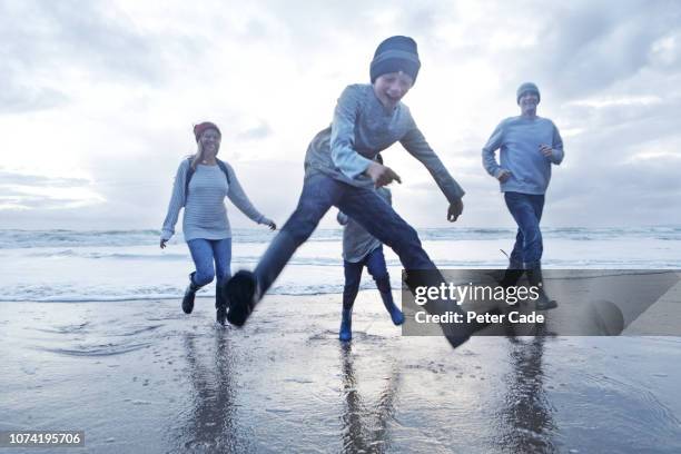 family playing at waters edge on beach in winter - family trip in laws stock-fotos und bilder