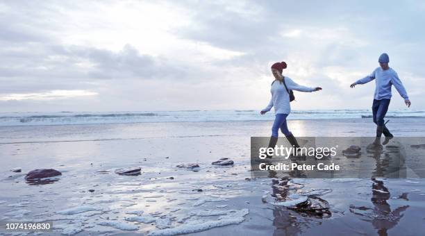 couple crossing stepping stones on beach - stepping stone stock-fotos und bilder