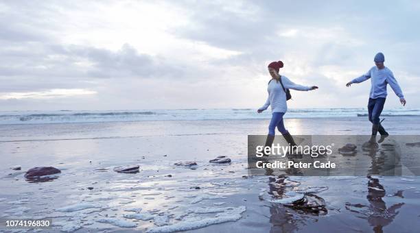 couple crossing stepping stones on beach - stepping stones stockfoto's en -beelden