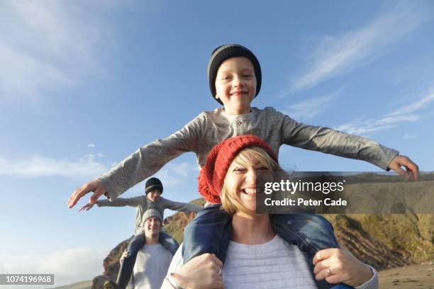 family on beach in winter, mother giving son piggyback - father in law stockfoto's en -beelden