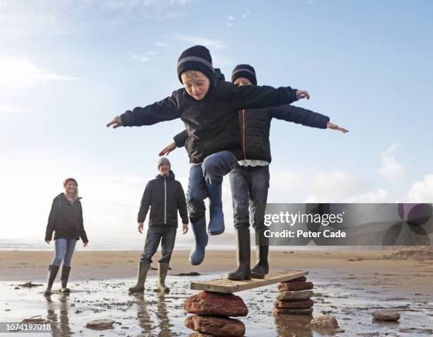 boys balancing on plank of wood, with family on beach - legal proceeding stock-fotos und bilder