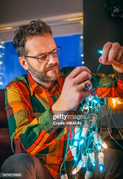 man trying to untangle christmas lights at home - tangled christmas lights stock pictures, royalty-free photos & images