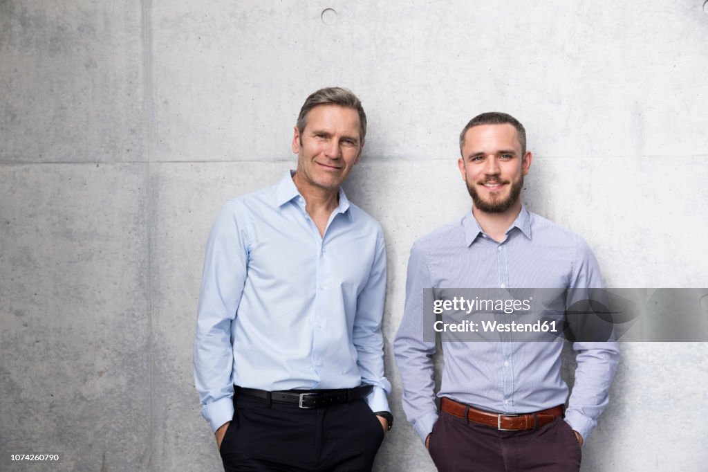 Portrait of two smiling businessmen at a wall