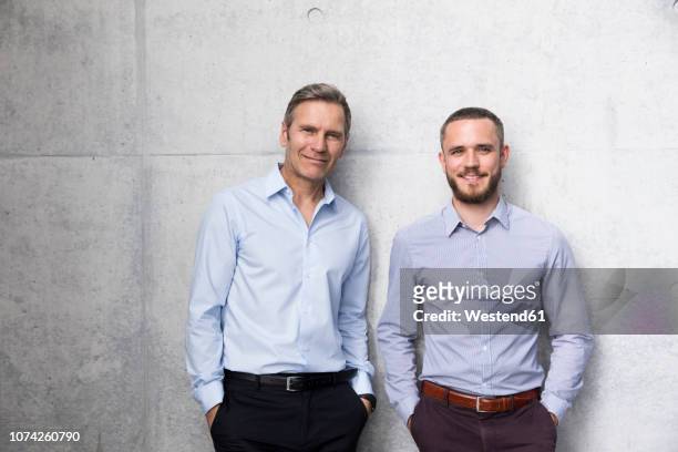 portrait of two smiling businessmen at a wall - due persone foto e immagini stock