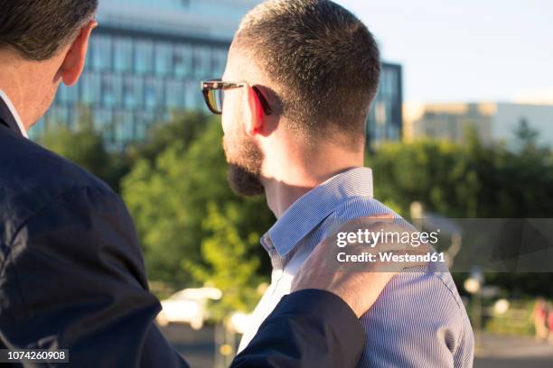 older businessman placing hand on shoulder of younger businessman - shoulder stock pictures, royalty-free photos & images