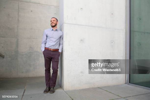 smiling businessman leaning against a wall - lässige kleidung stock-fotos und bilder