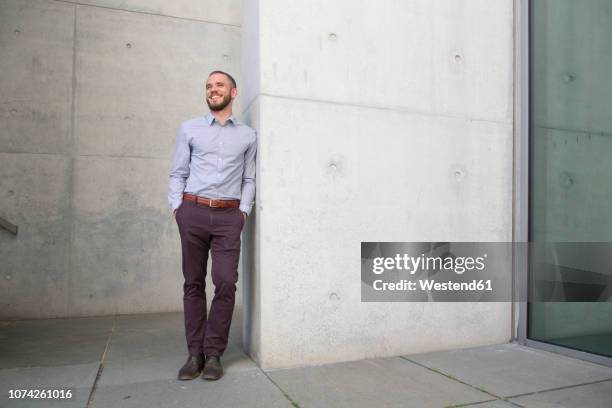 smiling businessman leaning against a wall - leunen stockfoto's en -beelden