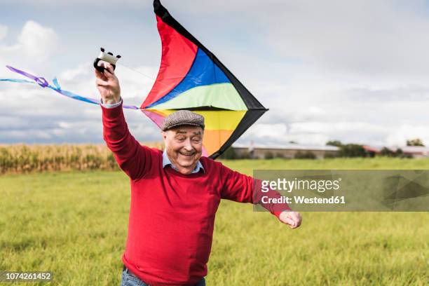 happy senior man flying kite in rural landscape - senior life active stock-fotos und bilder