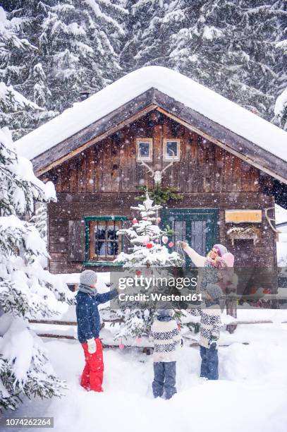 austria, altenmarkt-zauchensee, family decorating christmas tree at wooden house - christmas family tree stock-fotos und bilder