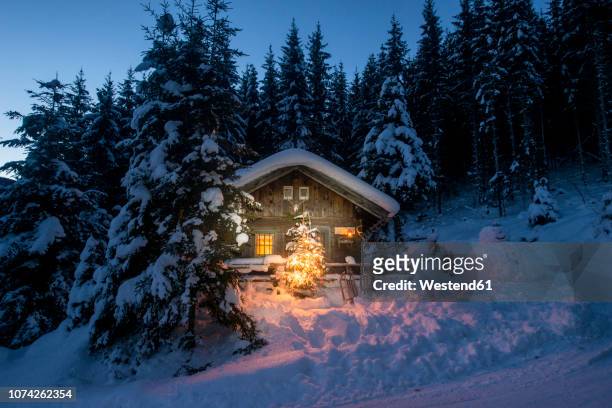 austria, altenmarkt-zauchensee, sledges, snowman and christmas tree at illuminated wooden house in snow at night - hut stock pictures, royalty-free photos & images