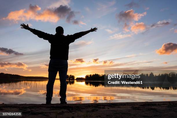 finland, kajaani, man watching sunset at the river with arms outstretched - finland stock pictures, royalty-free photos & images