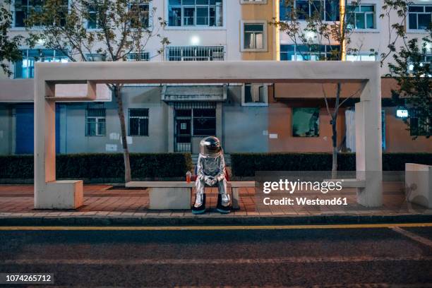 spaceman sitting on bench at a bus stop at night with soft drink - astronaut sitting stock pictures, royalty-free photos & images